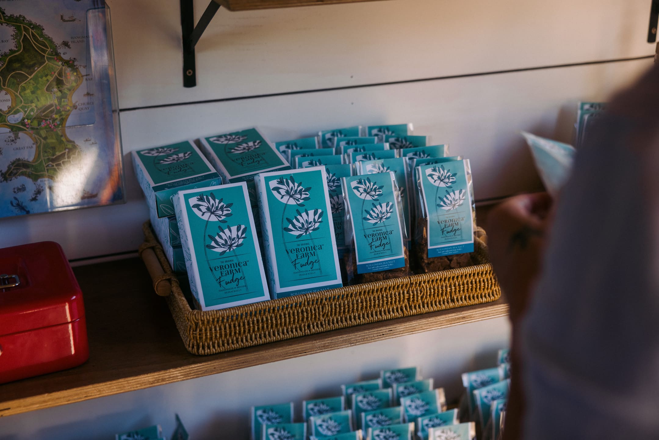 A wicker basket on a shelf holds several blue and white packages labeled Venomex Candy with a lotus flower illustration. A persons arm is partially visible on the right.